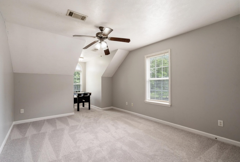 Carpeted room with a ceiling fan and sloped ceilings