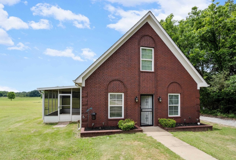 Brick exterior featuring a screened porch, gabled roofline, and front entry with wrought iron security door