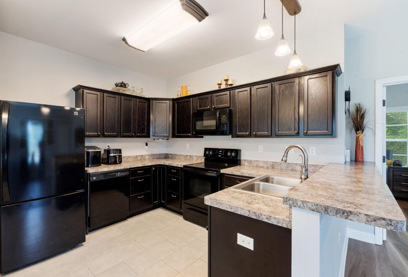 Kitchen featuring dark wood-finish cabinetry, black appliances, light-toned countertops, a double basin sink with a high-arc faucet, and pendant lighting