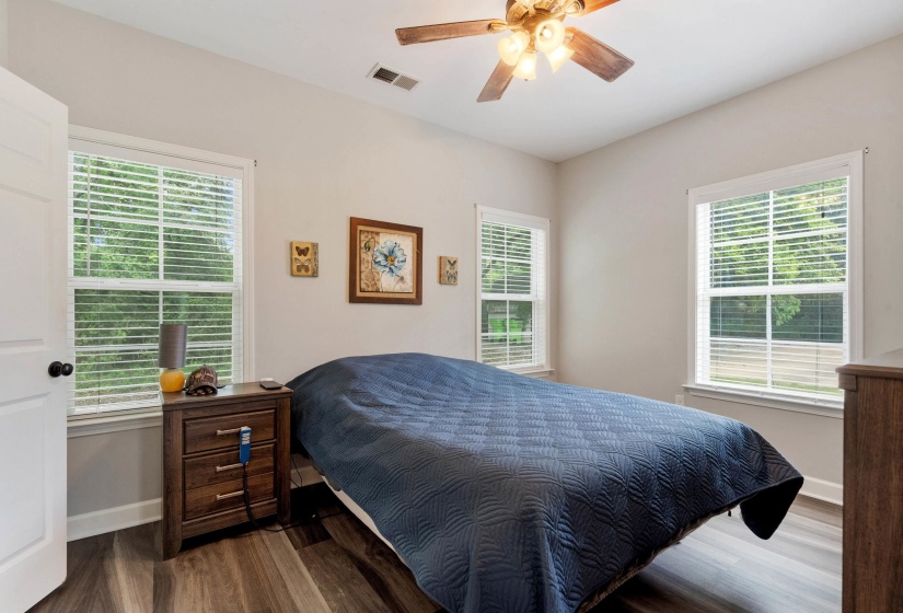 Bedroom featuring wood-finish flooring, a ceiling fan with integrated lighting, and two windows with blinds