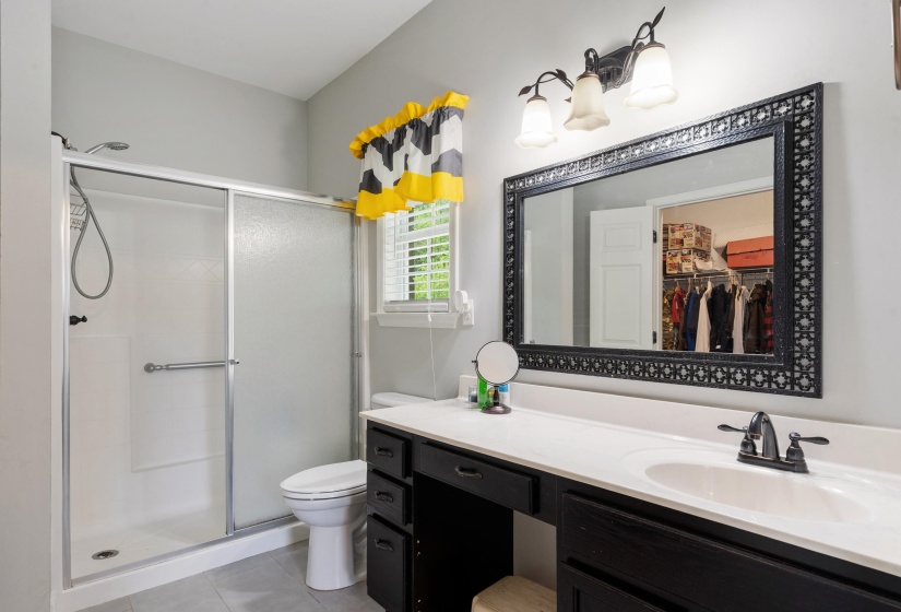 Bathroom featuring a shower with sliding glass doors, a single vanity with a white countertop and dark cabinetry, a vanity mirror with an ornate dark frame, and a three-light fixture