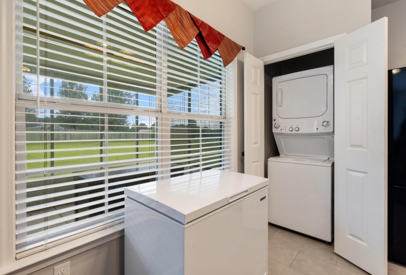 Utility area featuring a built-in stacked washer and dryer, tile flooring, and a large window with horizontal blinds