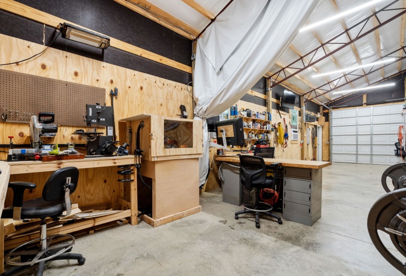 Spacious workshop featuring concrete flooring, a paneled overhead garage door, exposed beam ceiling with linear lighting, and integrated plywood wall paneling