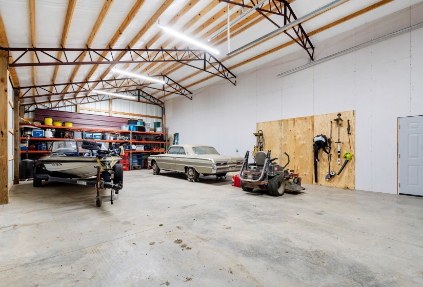 Spacious garage with high ceilings, exposed trusses, concrete flooring, and ample storage shelving
