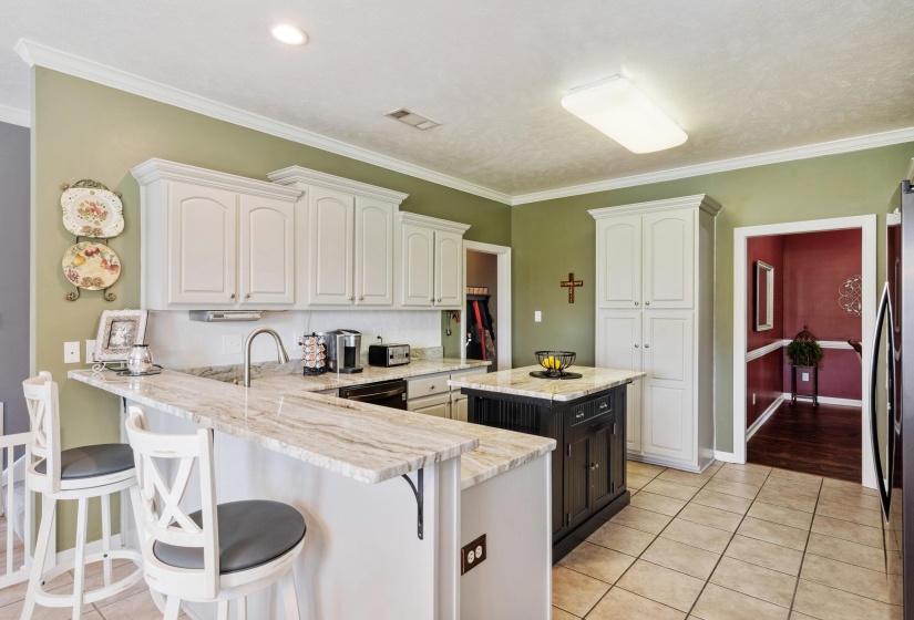 Kitchen featuring white upper and lower cabinetry, a center island with a dark wood-finish base, light-toned stone countertops, and tile flooring