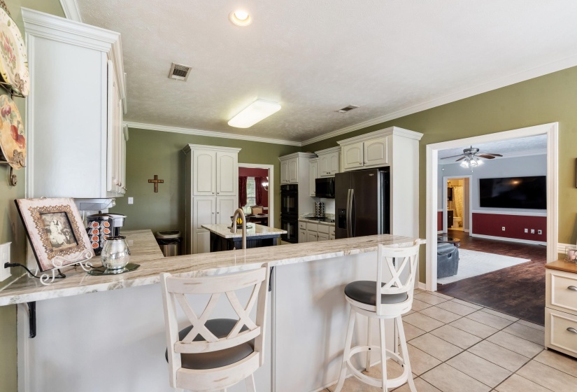 Kitchen featuring white cabinetry, stone-finish countertops, black appliances, and a central island with a sink
