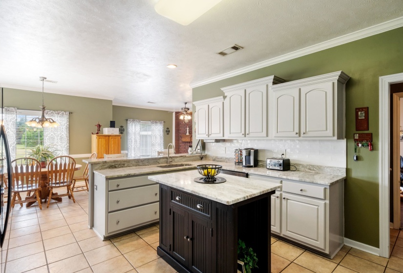 Kitchen featuring light-toned cabinetry, light granite countertops, a dark wood-finish island, and tile flooring