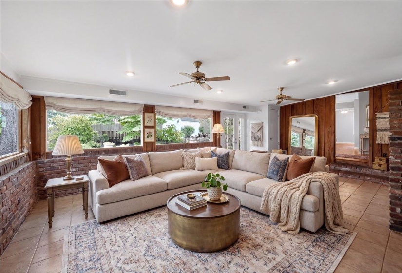 Spacious living area featuring floor-to-ceiling windows, exposed brick details, and wood paneling