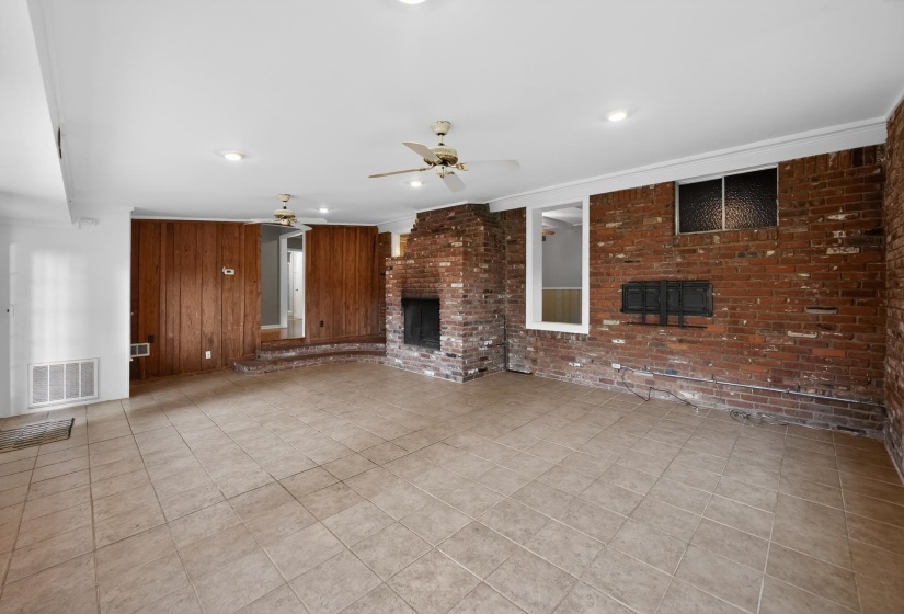 Spacious room featuring a prominent brick fireplace, light-toned tile flooring, and recessed ceiling lighting