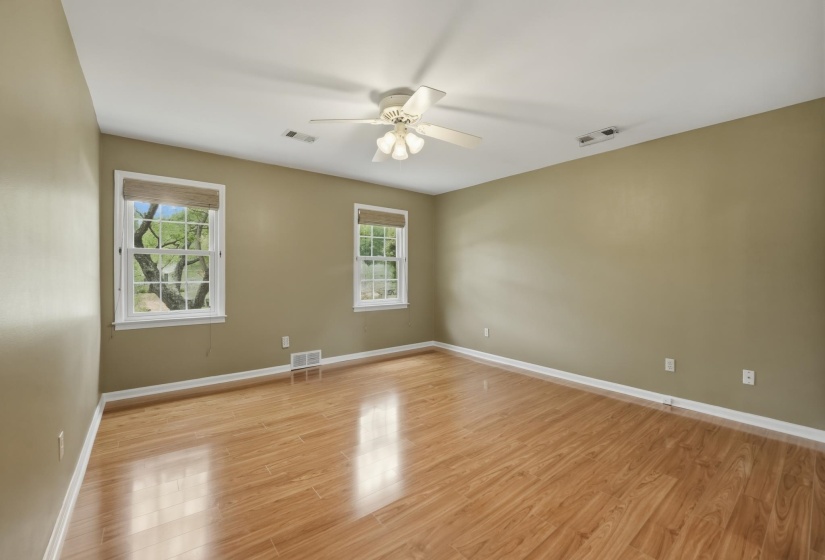 Spacious room with wood-finish flooring, two large windows with natural light, a ceiling fan with light fixture, and neutral-toned walls