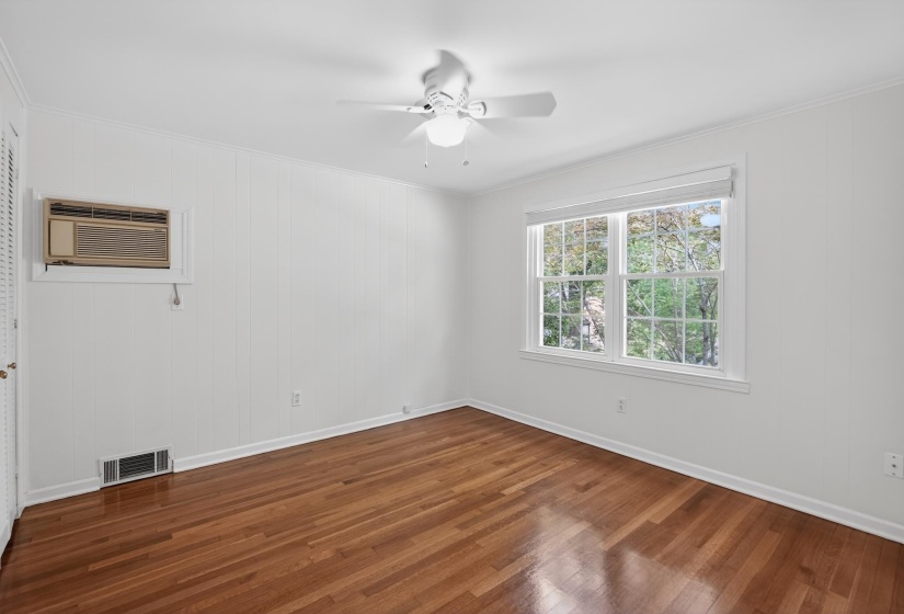 Bright room with wood-finish flooring, a double window, ceiling fan, white wall paneling, and baseboard trim
