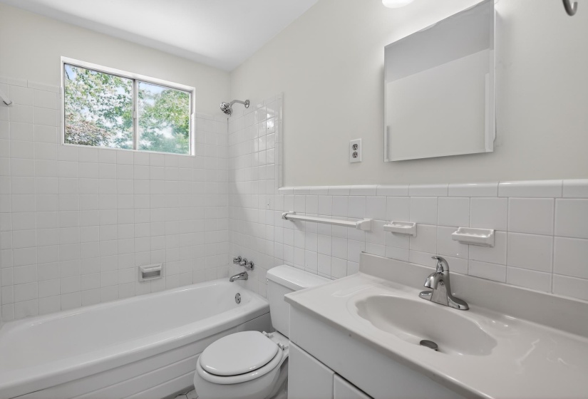 Bathroom with white tiled walls, a window above the bathtub, and a vanity with an integrated sink
