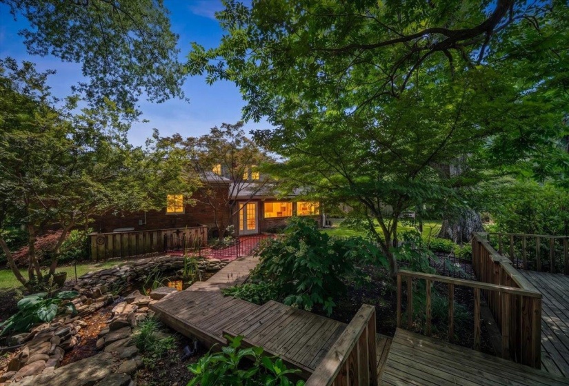 Expansive backyard featuring a multi-level wood deck, stone-lined water feature, and mature trees