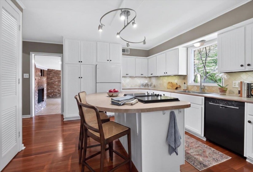Kitchen featuring wood-finish flooring, white cabinetry with black hardware, and an integrated cooktop on the peninsula