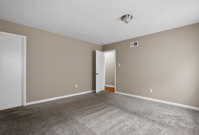 Carpeted room featuring neutral wall tones, white trim, a flush mount ceiling light, and an air vent
