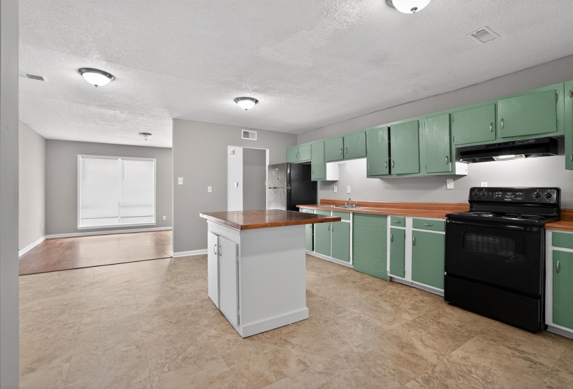 Open-concept kitchen featuring light green cabinetry, wood-finish countertops, and a central island with a wood-finish top