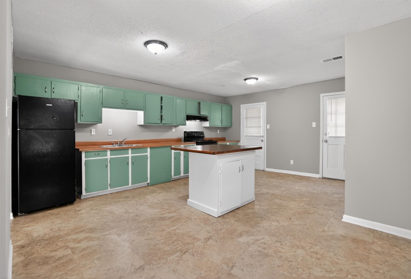 Kitchen featuring green cabinetry, wood-finish countertops, a central white island with wood-finish top, and black appliances