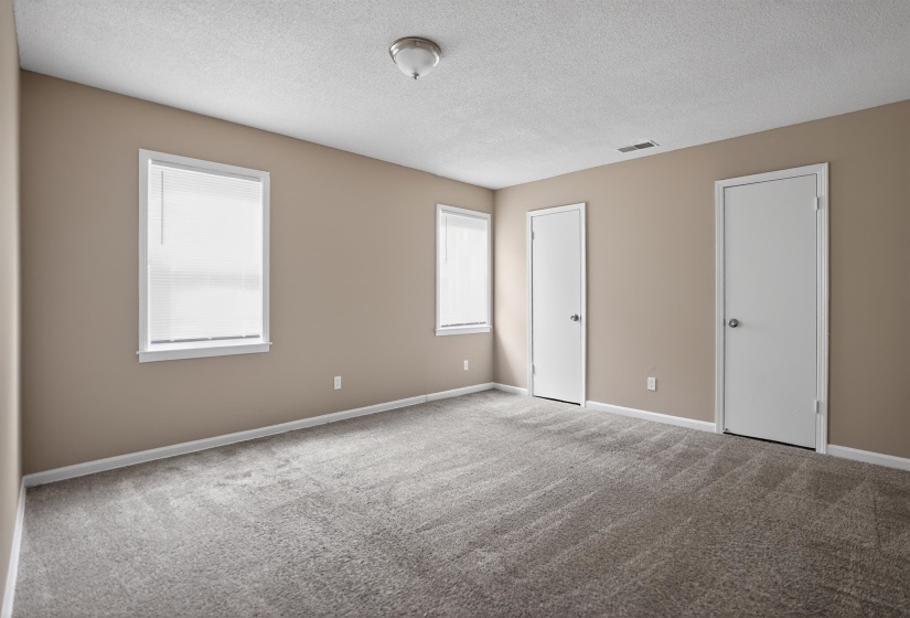 Spacious room featuring neutral paint, two windows with blinds, two white panel doors, and gray carpet flooring