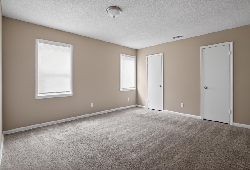 Spacious room featuring neutral-toned walls, grey carpeting, and two windows with white blinds
