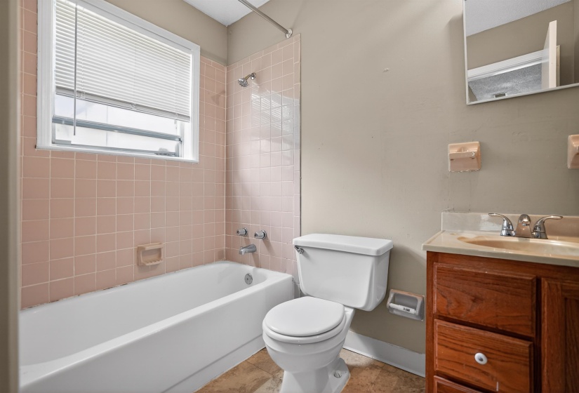 Bathroom featuring a full tub, pink tiled shower surround, window with blinds, toilet, and a vanity with a wood-finish cabinet