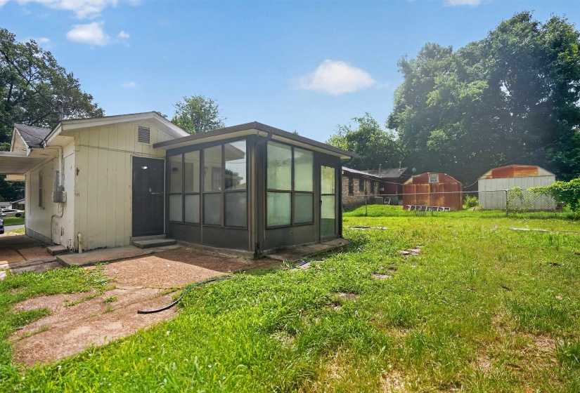 Rear exterior featuring a sunroom, carport, and expansive grassy yard