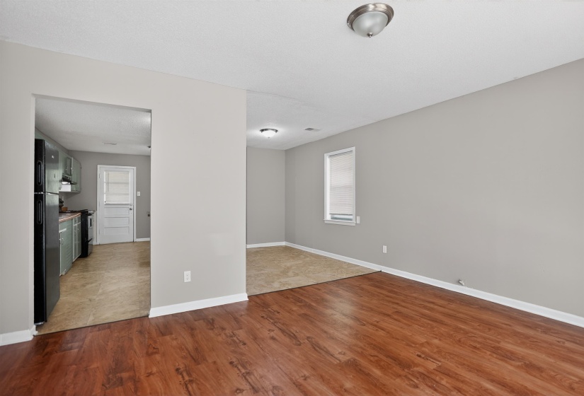 Open-concept living area featuring wood-finish flooring extending into a carpeted section, light gray wall paint, and a window with blinds