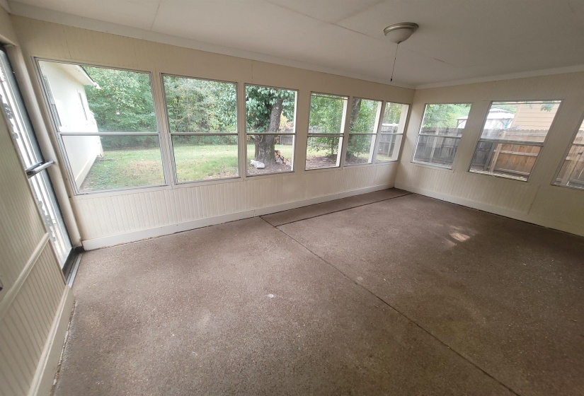 Screened-in porch featuring a concrete floor, beadboard wainscoting, numerous windows, and a ceiling-mounted light fixture