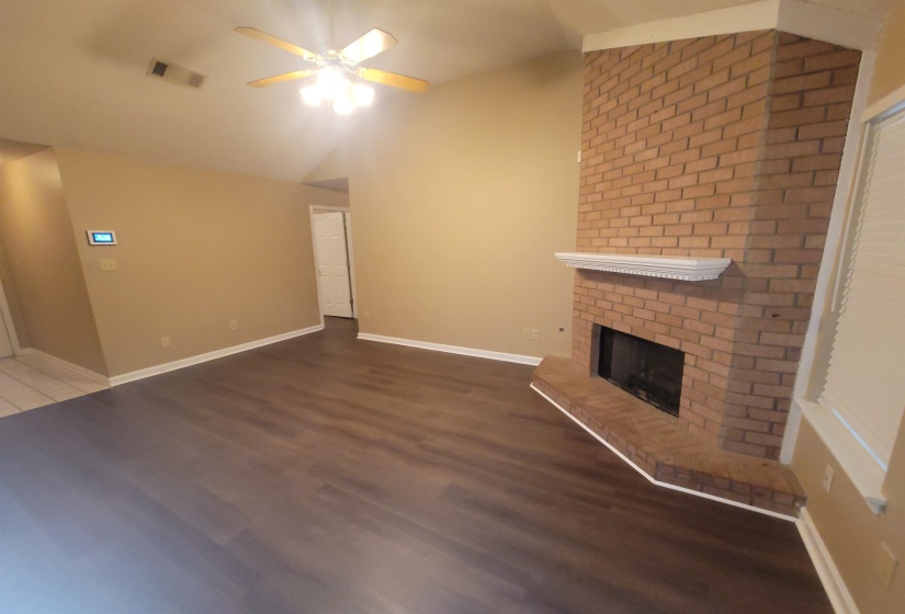Living area featuring wood-finish flooring, a brick-surround fireplace with a white mantel, and a ceiling fan with integrated lighting