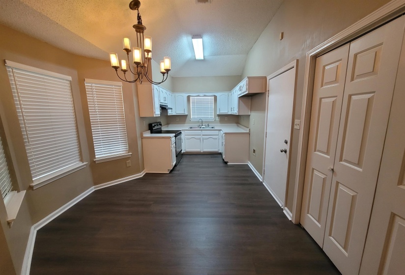 Open-concept kitchen and dining area featuring dark wood-finish flooring, white cabinetry, and light-toned countertops