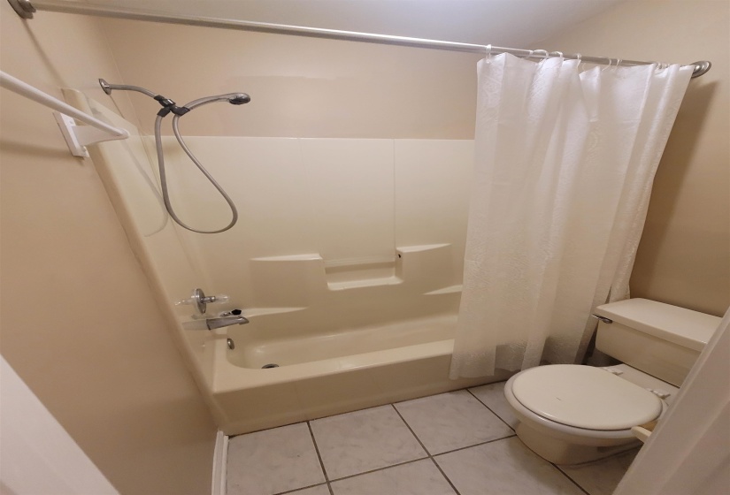 Bathroom featuring a tub/shower combination with a handheld showerhead, a toilet, and tiled flooring