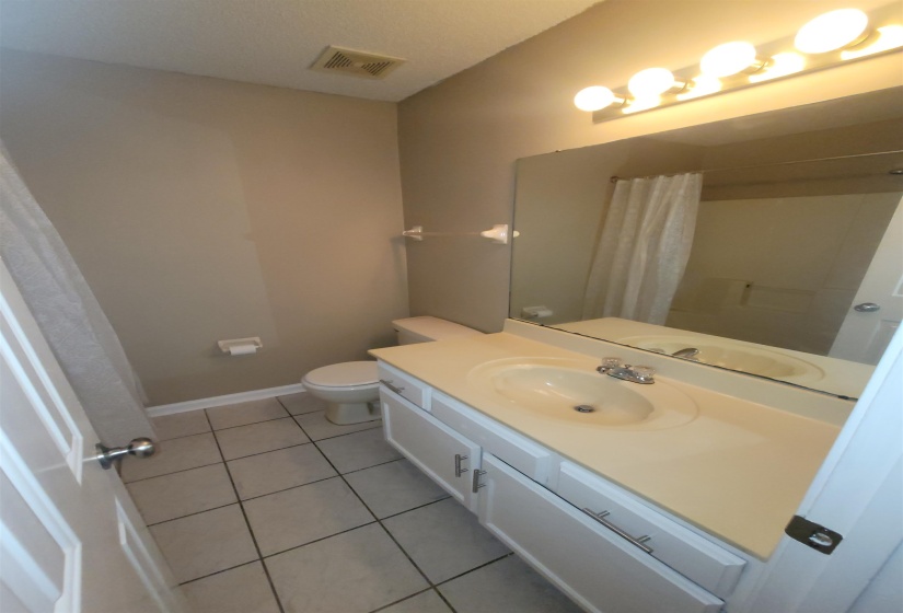 Full vanity with integrated sink and chrome faucet, set against a large mirror with a four-bulb vanity light fixture