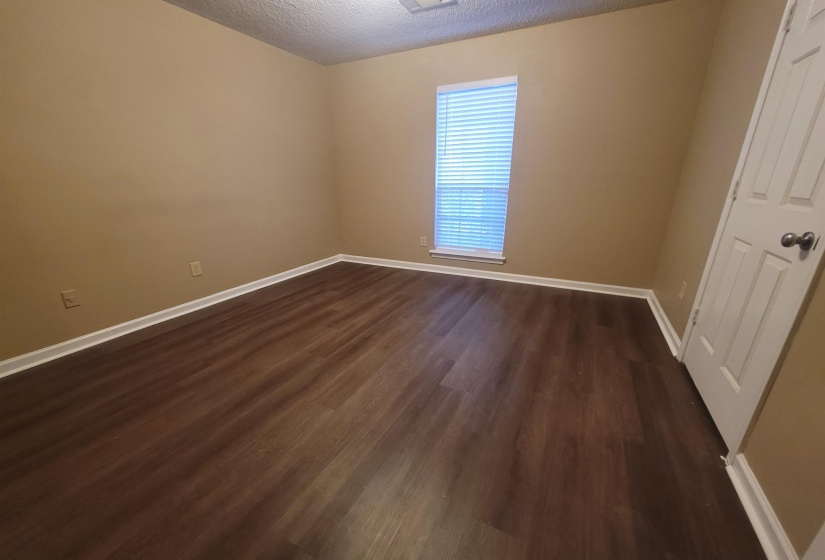 Room featuring dark wood-finish flooring, light tan walls, white baseboards, a single window with blinds, and a white paneled door