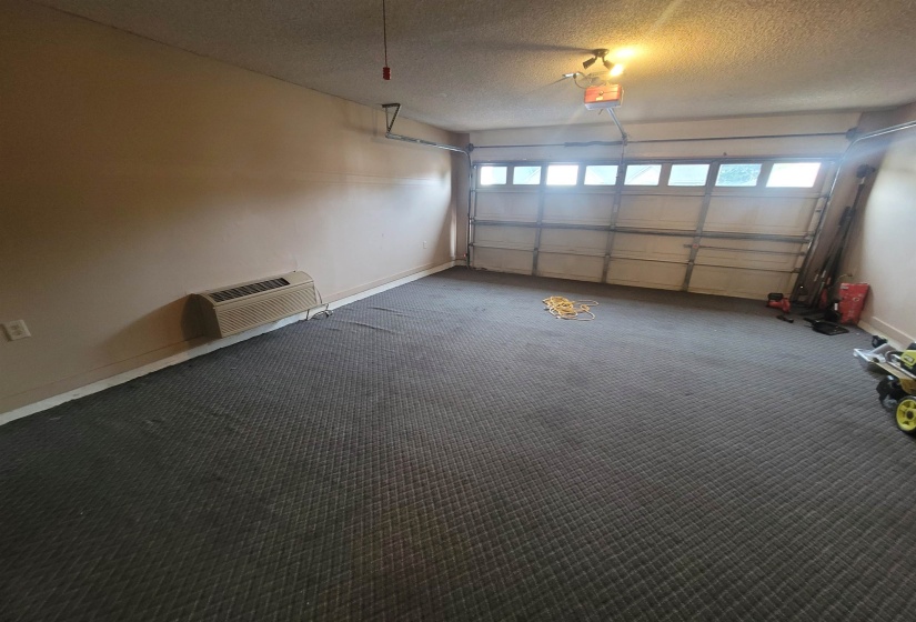 Spacious garage featuring a paneled overhead door with integrated windows, textured ceiling, wall-mounted heating unit, and patterned carpet flooring