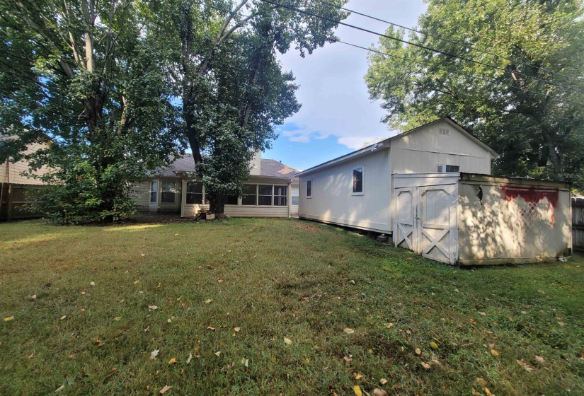 Expansive backyard with a manicured lawn, mature trees, a detached storage shed, and an enclosed patio with multiple windows