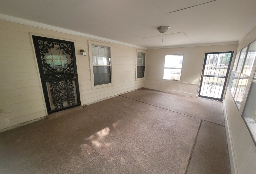 Enclosed porch with a concrete floor, featuring a ceiling-mounted light fixture, white wood-paneled walls, and multiple windows