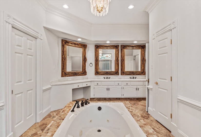 Jetted soaking tub with a white vanity featuring dual sinks, ornate framed mirrors, and a dedicated vanity seating area