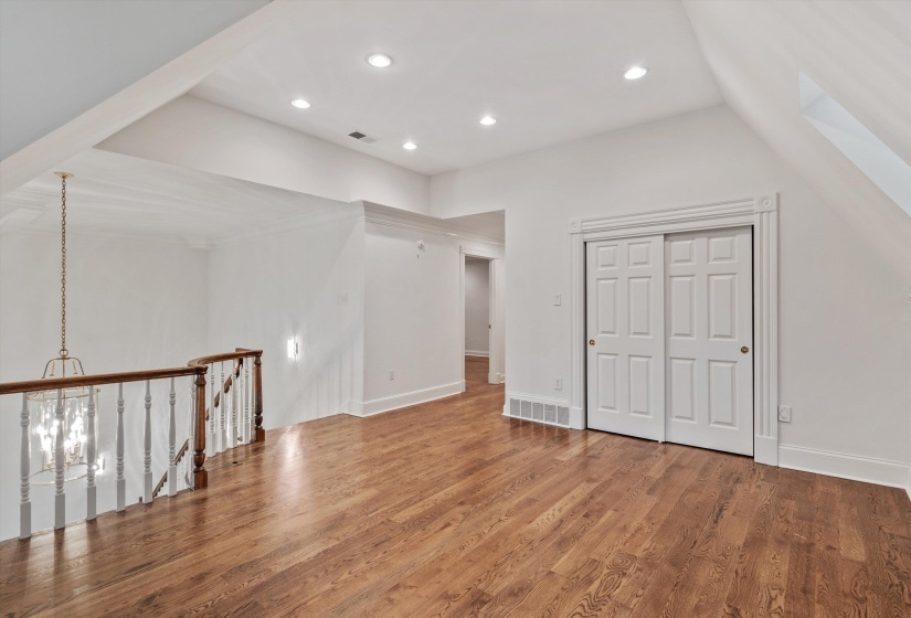 Upper-level room featuring hardwood flooring, recessed lighting, white walls, a white-painted railing with wood-finish top, and sliding white paneled closet doors