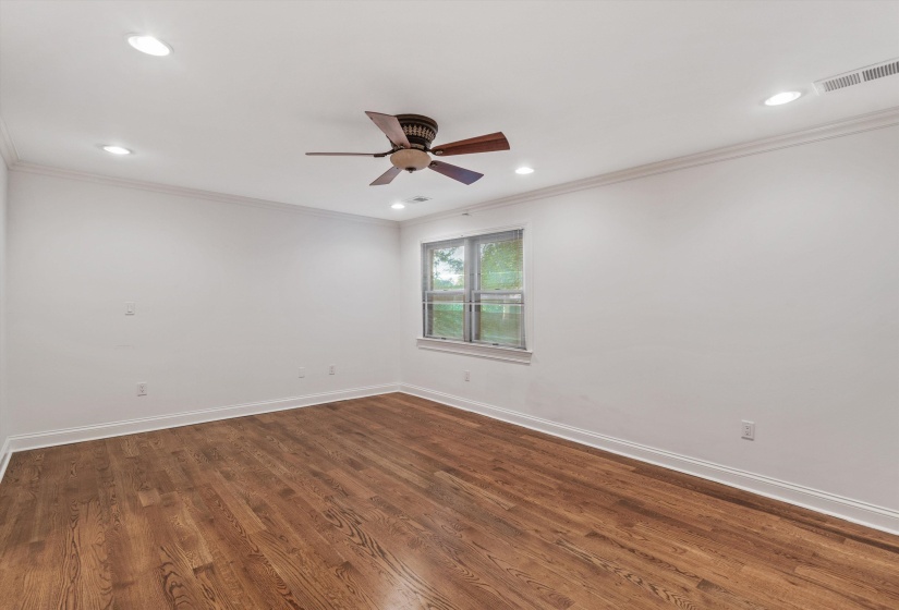Spacious room featuring wood-finish flooring, white walls, and a ceiling fan