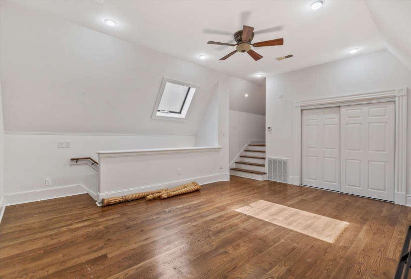 Spacious room featuring wood-finish flooring, a ceiling fan, recessed lighting, and a skylight