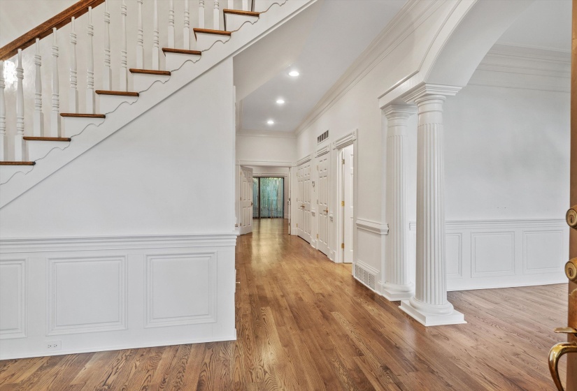 Entryway featuring wood-finish flooring, wainscoting, a balustrade staircase, recessed lighting, and a decorative arched doorway with fluted columns