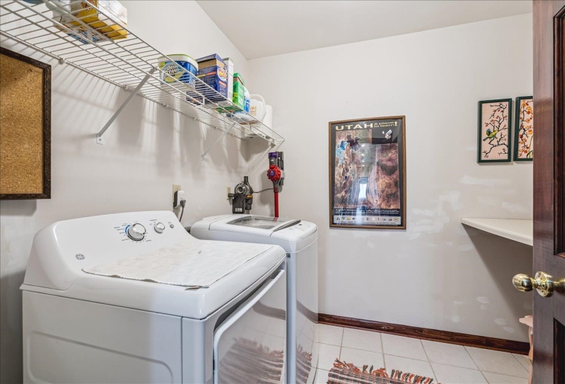 Dedicated laundry area featuring a white top-load washing machine and dryer, overhead wire shelving for storage, and a corner wall-mounted shelf