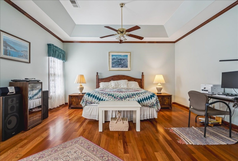 Room featuring wood-finish flooring, a tray ceiling, crown molding, and a ceiling fan