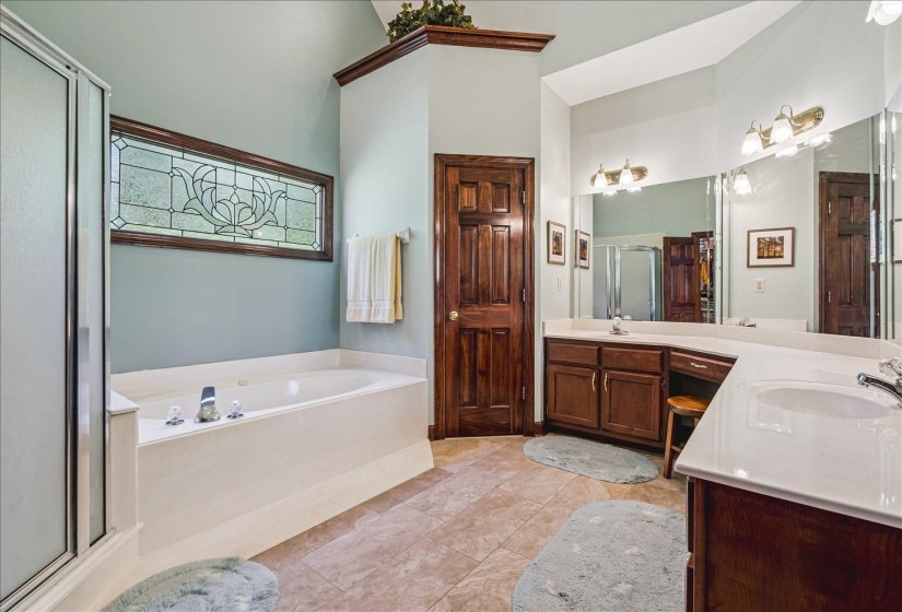 Spacious bathroom featuring a built-in soaking tub with a decorative privacy window, a walk-in shower with a glass enclosure, two separate vanity sinks with integrated mirrors, and warm wood cabinetry