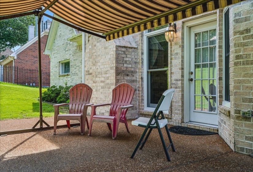 Outdoor patio featuring a striped awning, brick exterior, and a glass-paneled door