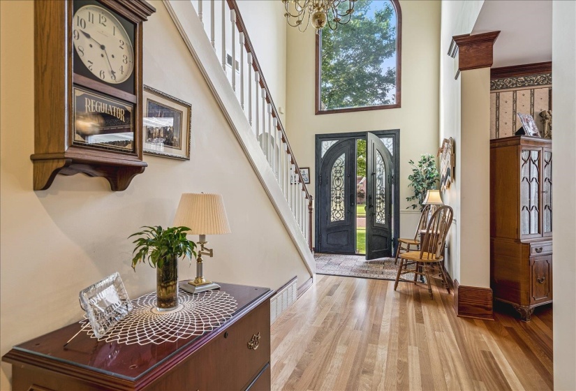 Two-story foyer featuring hardwood flooring, a grand staircase with white balusters, and a large arched window above double entry doors with decorative glass inserts