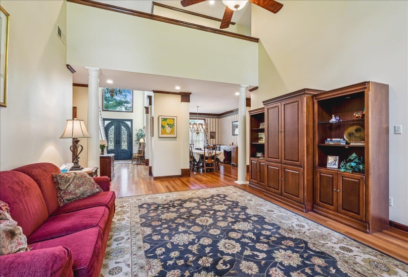 Two-story living area featuring a vaulted ceiling with a ceiling fan, wood-finish flooring, and decorative columns