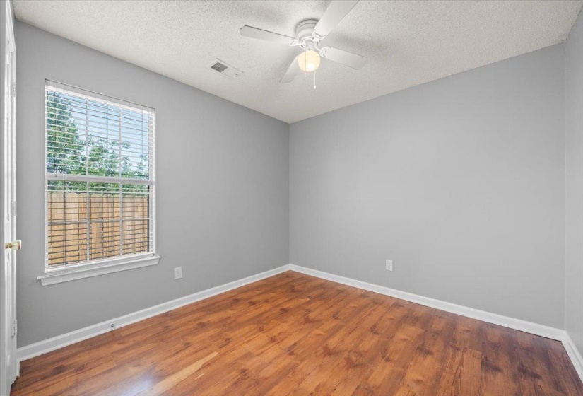 Room featuring wood-finish flooring, a ceiling fan with integrated lighting, and a window with blinds