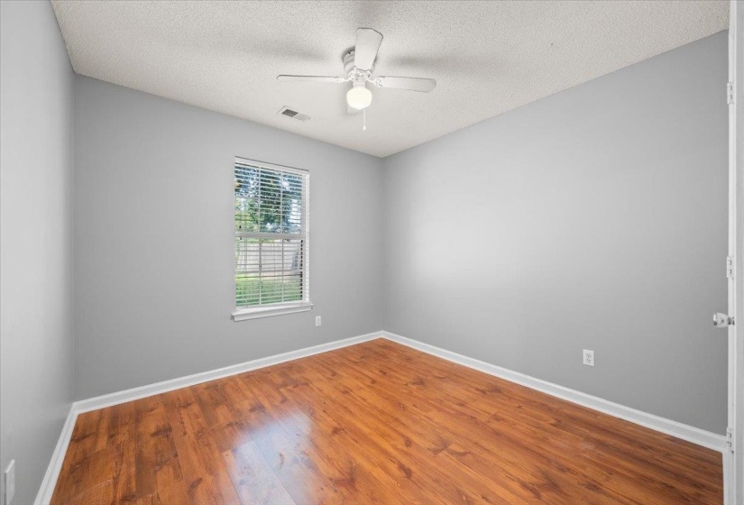 Spacious room featuring wood-finish flooring, light gray wall tones, a ceiling fan with integrated lighting, and a window with blinds