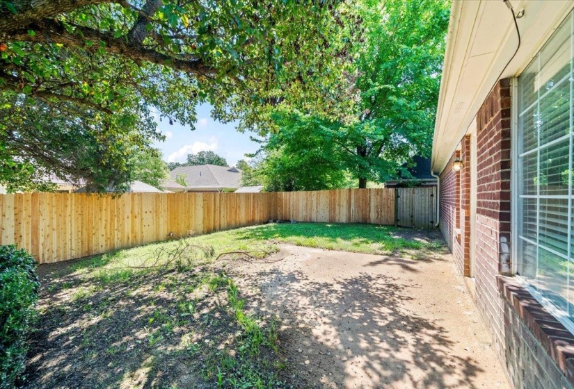 Expansive backyard featuring a new wood privacy fence, mature shade trees, and a brick exterior with a large window