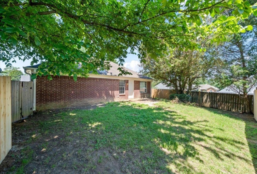 Expansive backyard featuring a brick exterior, partial fencing, mature trees, and a grassy area